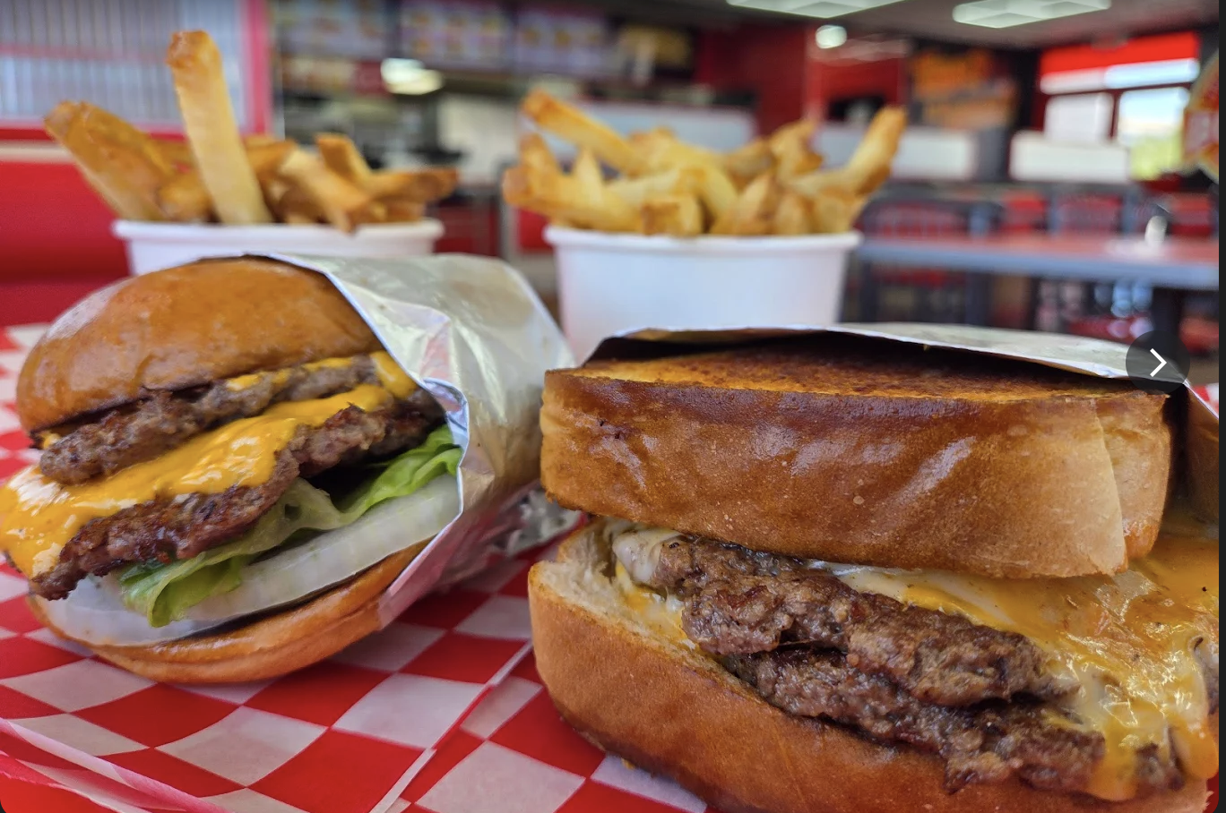 Two double smash cheeseburgers with cups of hand-cut fries on red checkered paper in the dining room