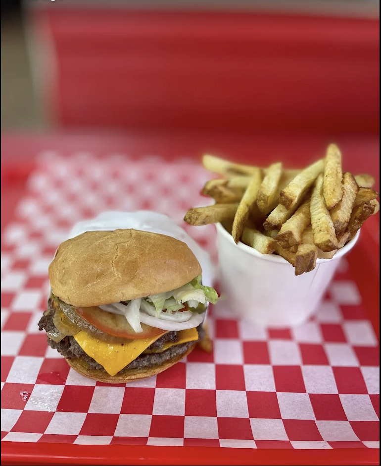 A loaded smash burger and a generous cup of fries on a red tray over black-and-white checker