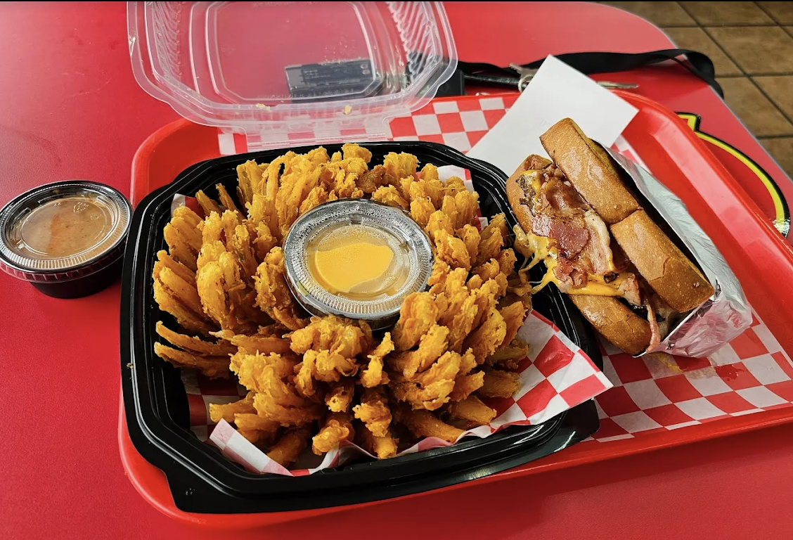 The Best Bomb Classic breaded blooming onion with dipping sauce beside a sandwich on a red tray