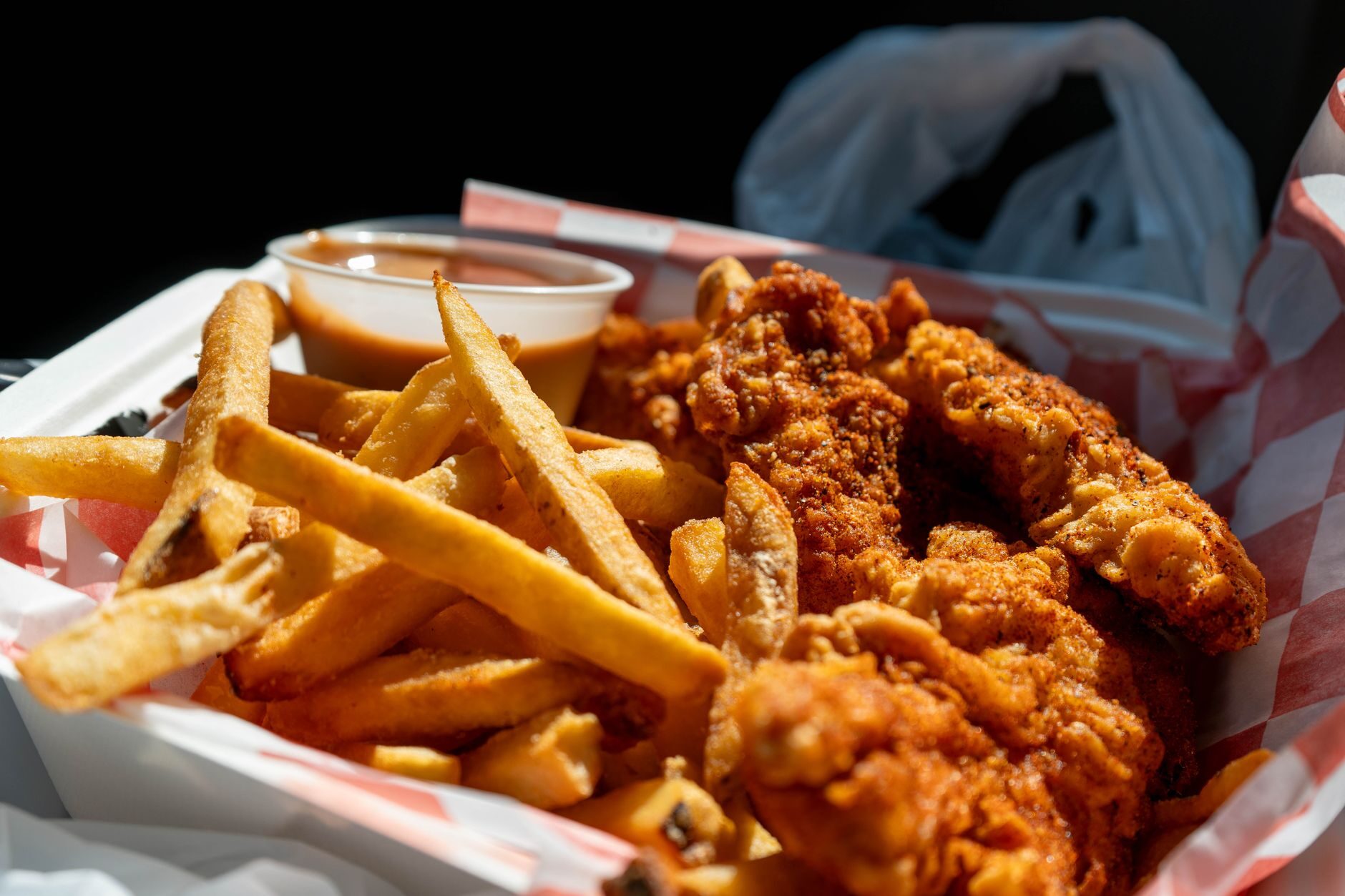 Crispy chicken tenders and fries with dipping sauce in a red-and-white checkered basket