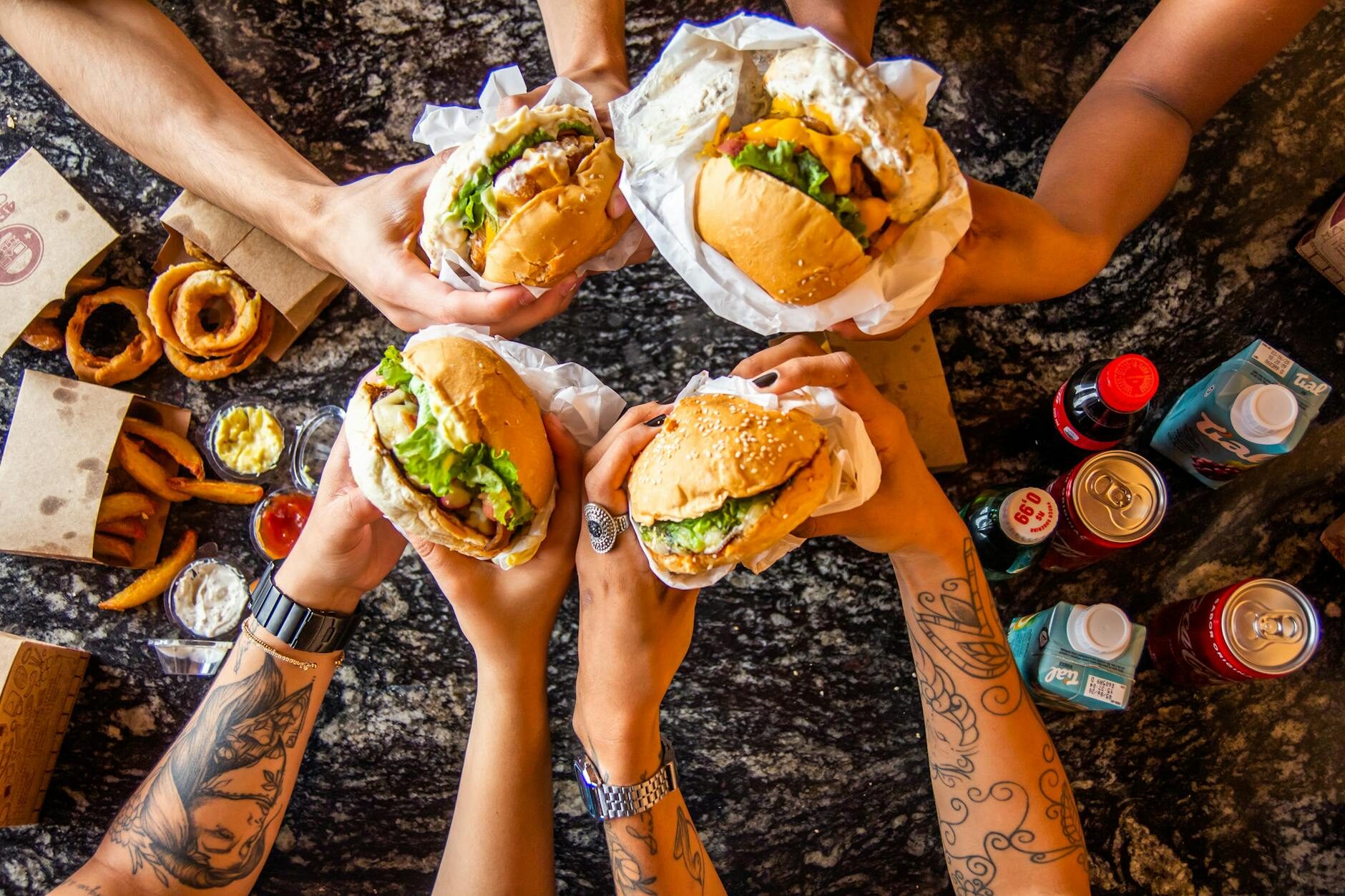 Four friends raising burgers together over a table of onion rings and fries