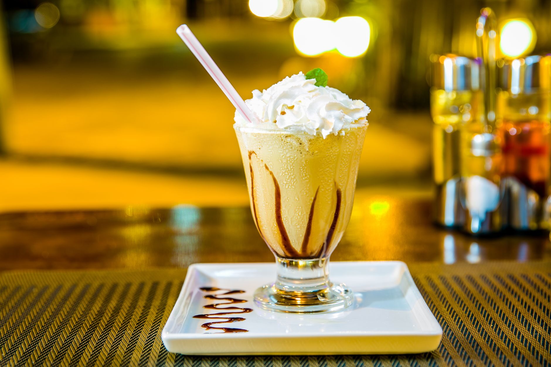 A classic shake topped with whipped cream and chocolate drizzle under warm light